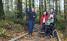 A CRD parks employee points to a tree during a guided tour, while a family of three watches.